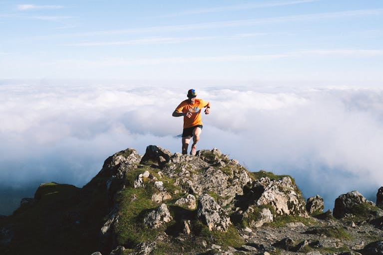 Man running on rocky mountain peak above the clouds, symbolizing achievement and adventure.